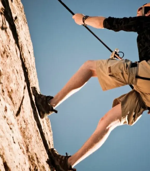 Adventurer rappelling down a vertical wall with safety gear
